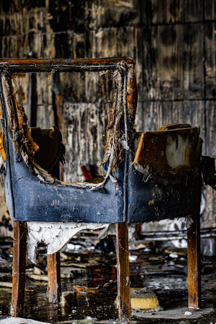 why-choose-us A worn, burnt chair in an old, abandoned room with peeling walls.