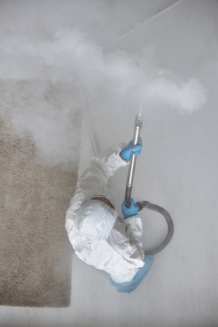 Person in protective gear fumigating indoors with steam equipment.